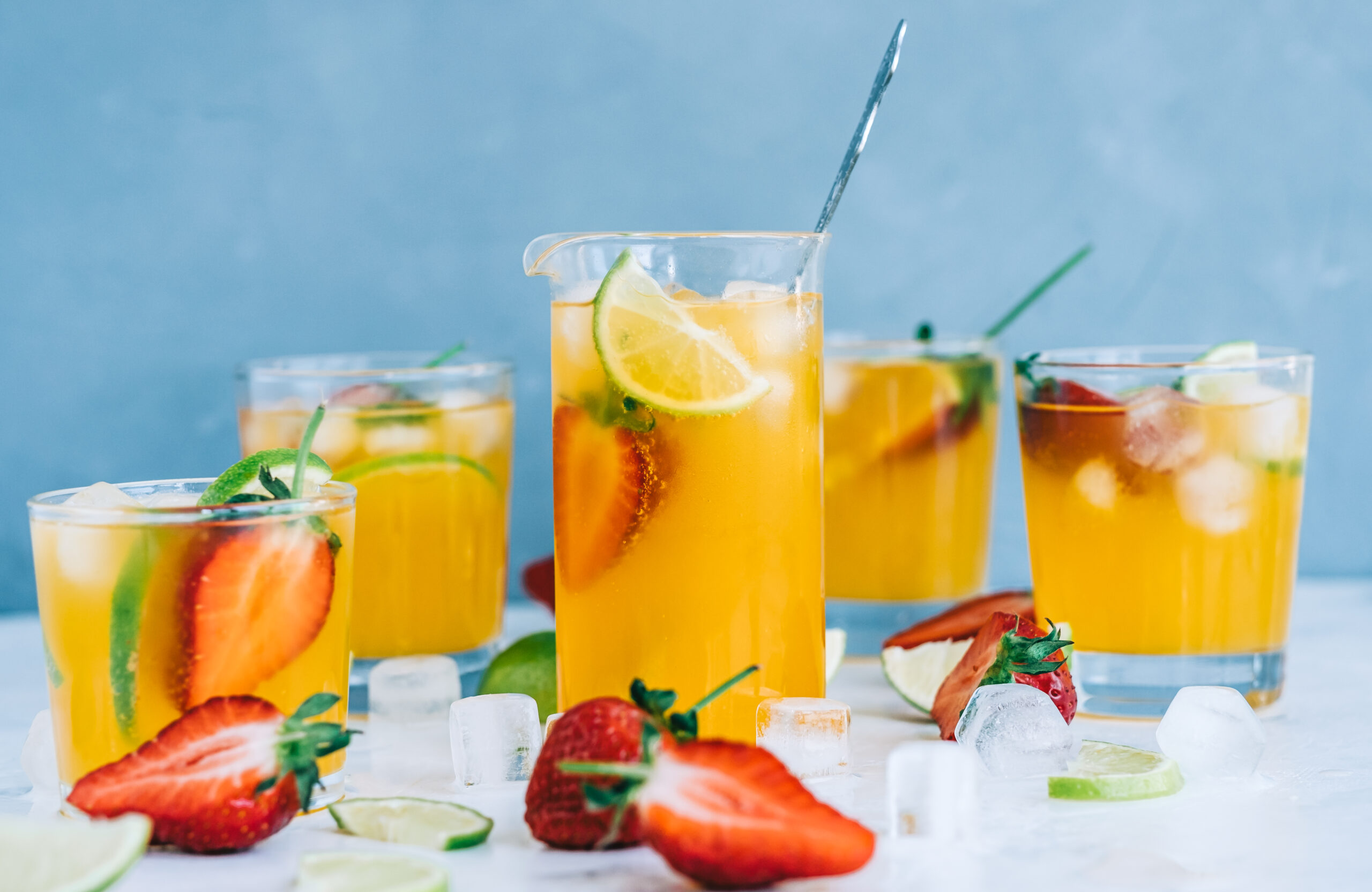 Verre de punch pour 30 personnes décoré avec une tranche d'orange, entouré de fruits et d'une bouteille de rhum